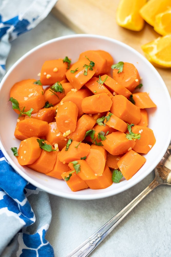 Bowl of glazed carrots next to oranges.
