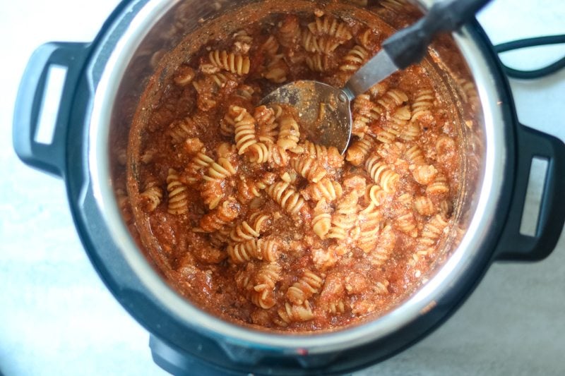 Creamy tomato sauce on rotini noodles in instant pot with silver spoon in sauce