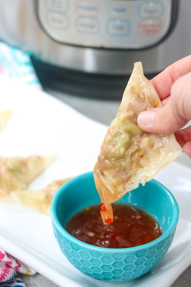 Potsticker being dipped into blue bowl of homemade sweet chili sauce
