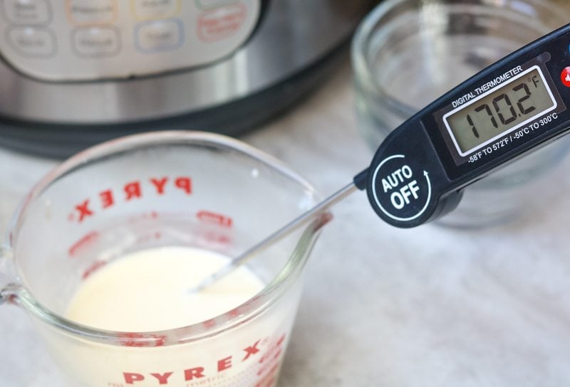 A digital thermometer inserted into a glass measuring cup of warm cream. Temperature reads 170