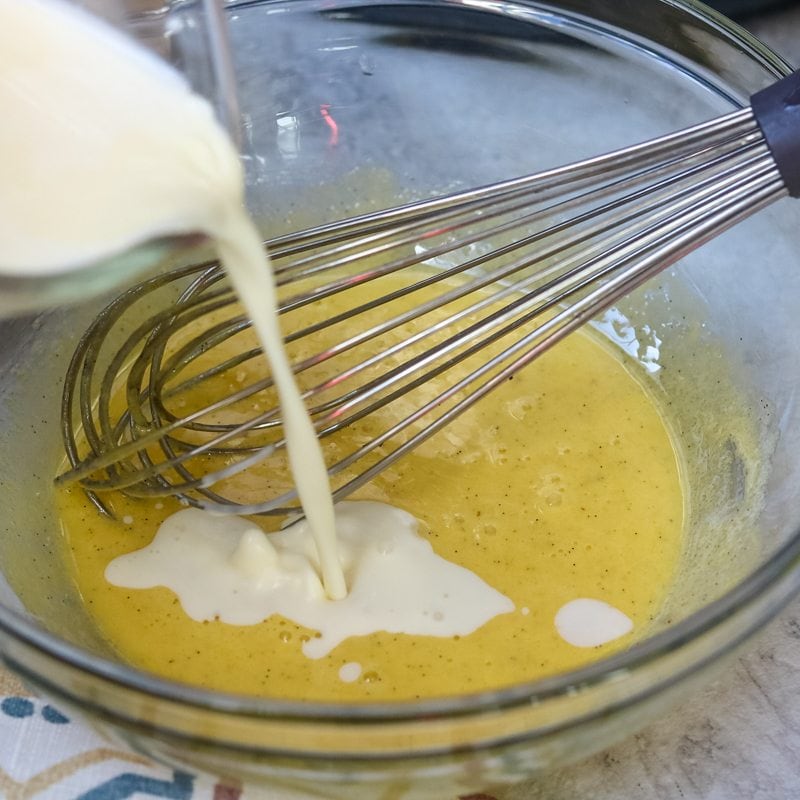 Warm cream being poured into the eggs and sugar with whisk to side