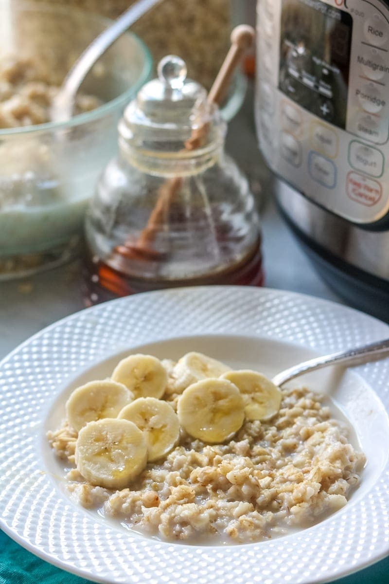 Instant Pot next to white bowl filled with creamy oatmeal topped with sliced bananas