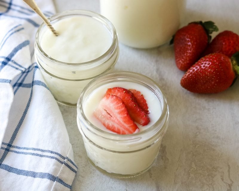 3 small glass jars filled with homemade yogurt. One topped with sliced strawberries