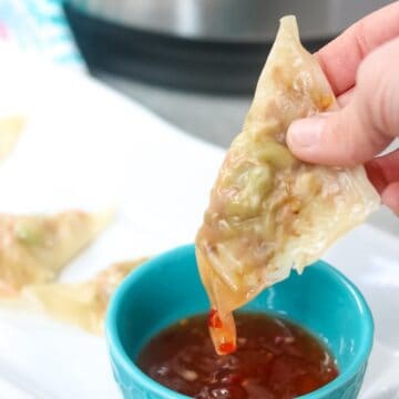 Dipping steamed wonton filled with vegetables in asian chili sauce