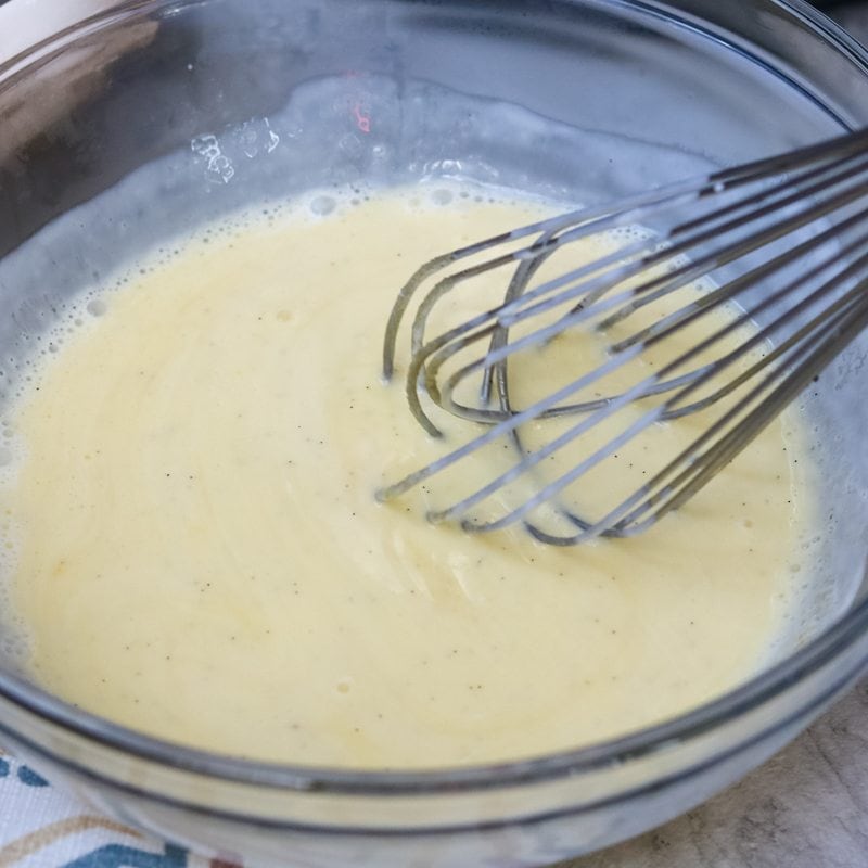 A metal whisk whisking the custard in a glass bowl