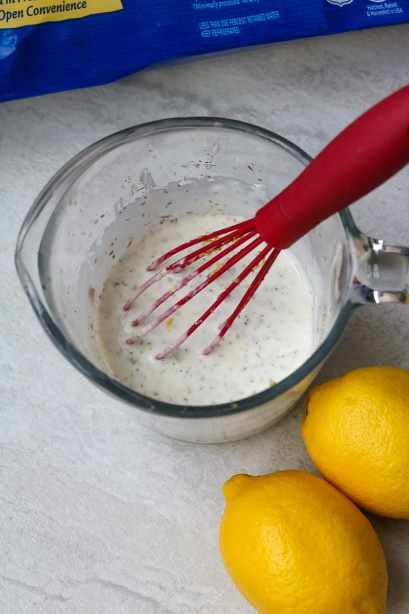 Glass measuring cup filled with greek yogurt greek marinade with lemon to side.