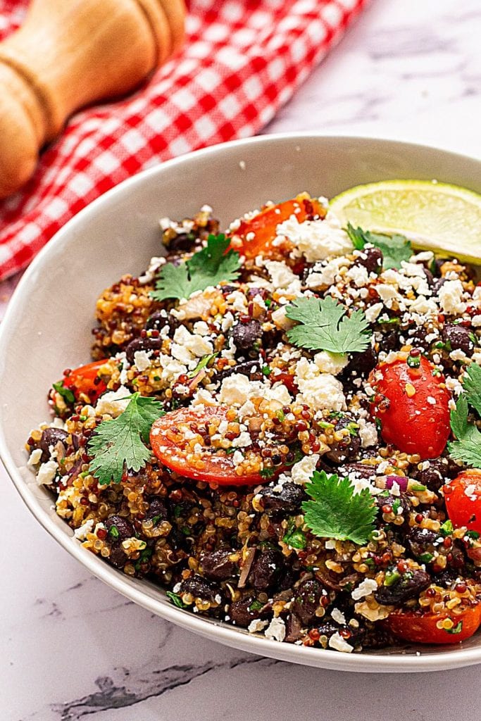Gluten Free Mexican Quinoa Salad in white bowl topped with feta and cherry tomatoes.