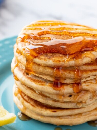 Stack of whole wheat pancakes on plute plate topped with syrup
