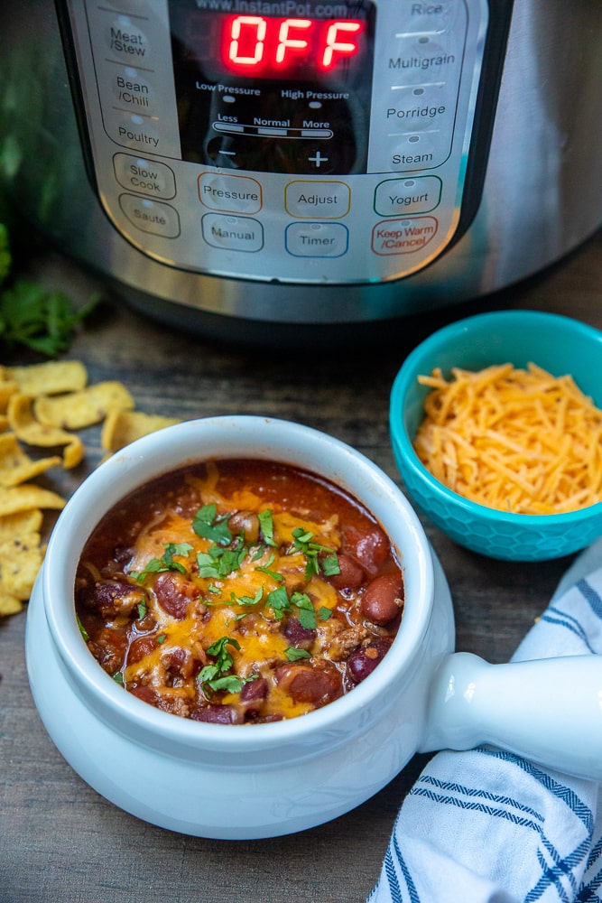 Instant Pot Classic Beef Chili in red bowl next to pressure cooker.