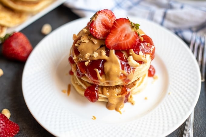 Peanut Butter Pancakes on white plate with strawberry sauce and fresh strawberries.