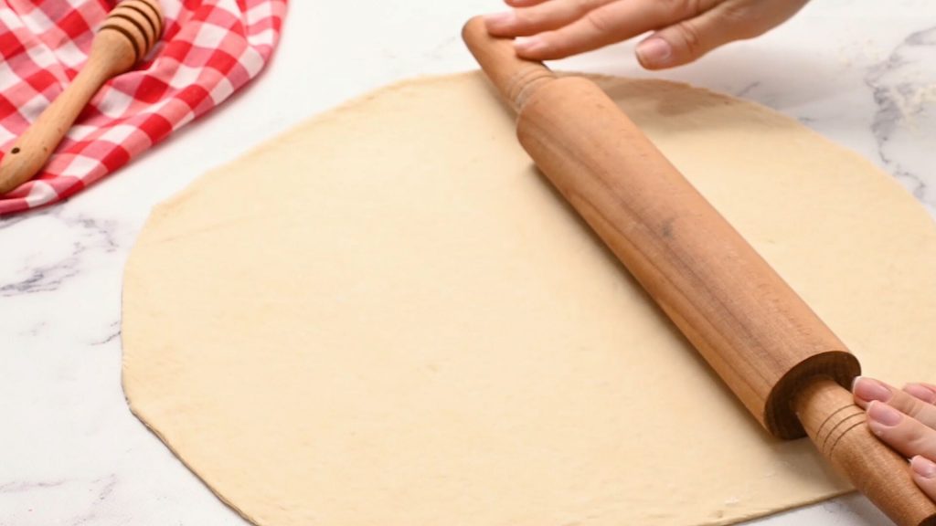 Pizza Dough Being rolled out on white counter.