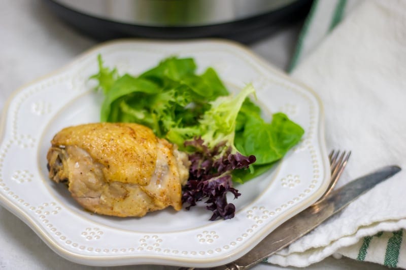 Instant Pot Chicken Thigh on white plate next to salad