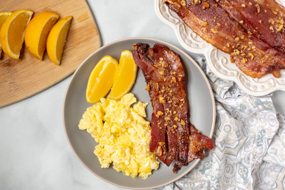 Candied Bacon on plate with scrambled eggs and oranges. 