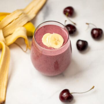 Cherry Smoothie in clear glass with sliced bananas on top and fresh cherries in background.glass with sliced bananas and fresh cherries in background.