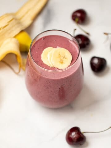 Cherry Smoothie in clear glass with sliced bananas on top and fresh cherries in background.glass with sliced bananas and fresh cherries in background.