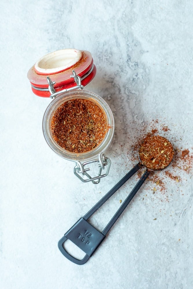 Spice jar with homemade Cajun Seasoning next to measuring spoon.