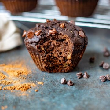 Chocolate Zucchini Muffin with bite out of it next to chocolate chips and cocoa powder