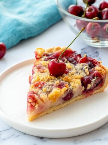 Slice of Cherry Pie on White Plate with fresh cherry on top