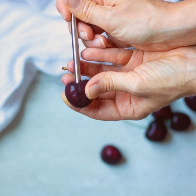 Hand holding a fresh cherry, using a straw to pit cherries.