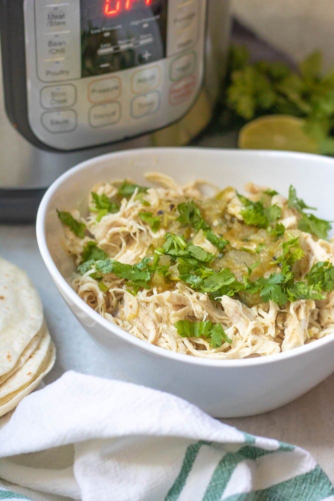 Instant Pot Shredded Mexican Chicken in white bowl topped with cilantro next to instant pot