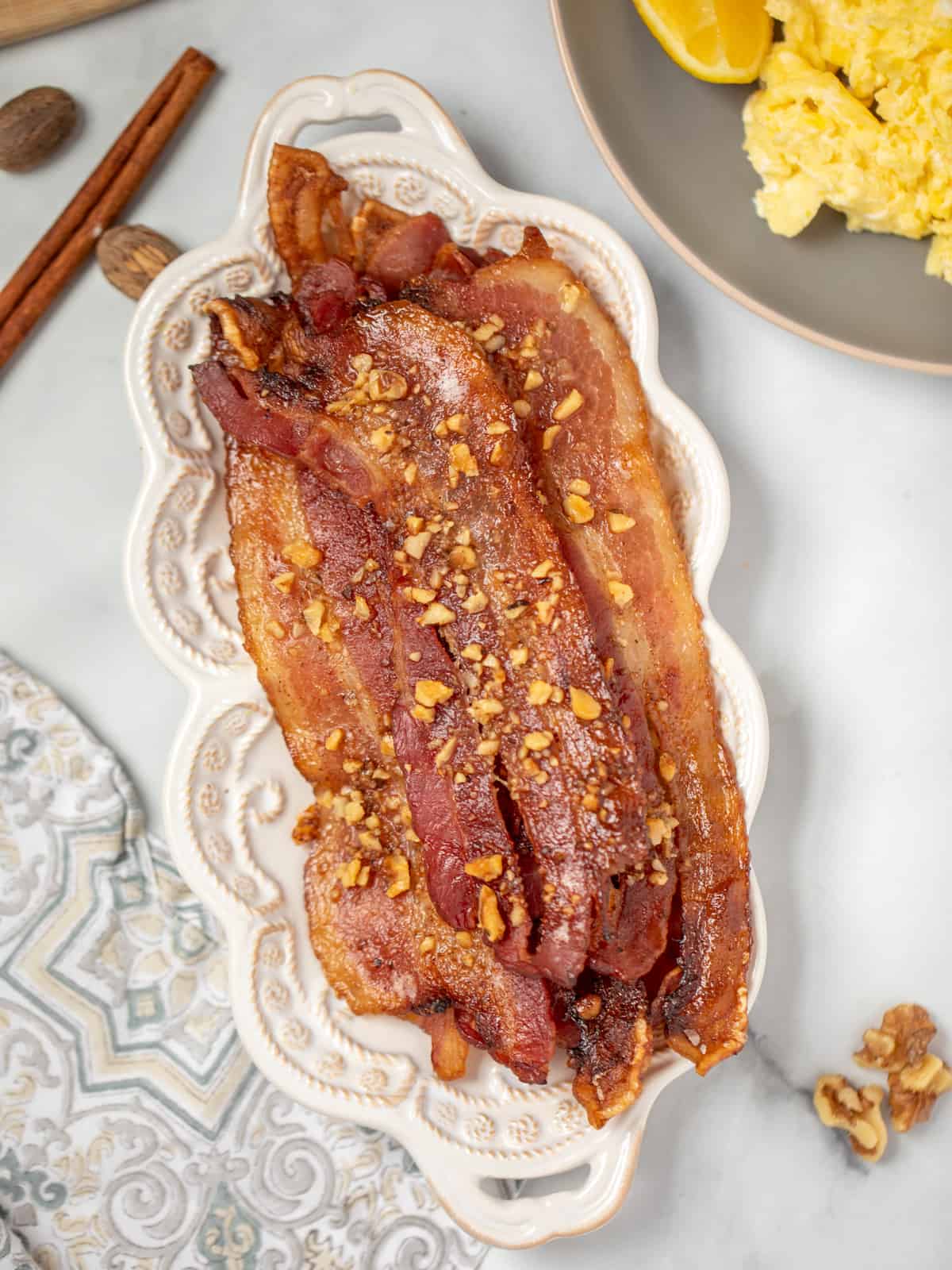 Candied Bacon on white serving platter next to scrambled eggs. 