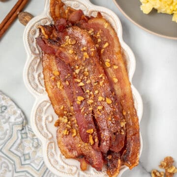 Candied Bacon on white serving platter next to scrambled eggs.