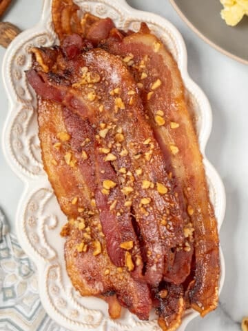 Candied Bacon on white serving platter next to scrambled eggs.