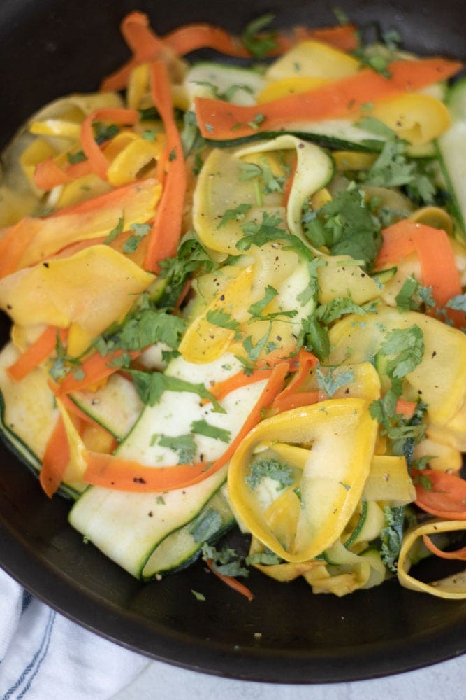 Zucchini, yellow squash and carrot ribbons sauted in pan.