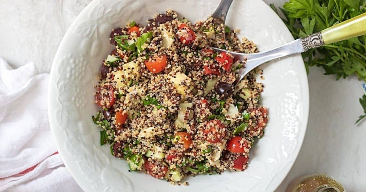 Bowl of greek quinoa salad with seving spoons.