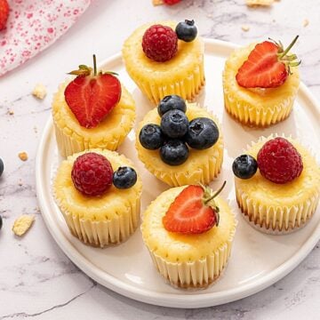 Mini Muffin tin cheesecakes on white platter topped with fresh berries
