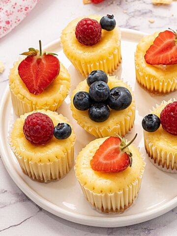 Mini Muffin tin cheesecakes on white platter topped with fresh berries