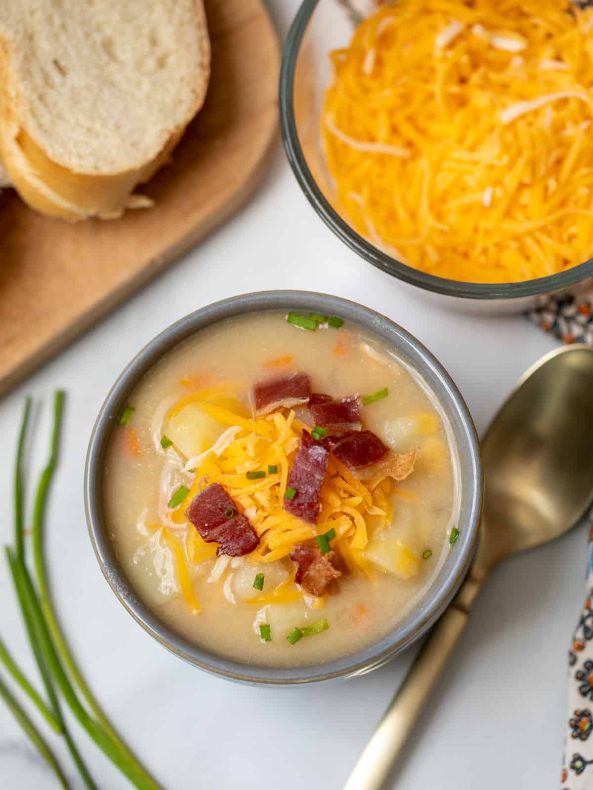 Bowl of potato soup topped with cheese and bacon next to sliced bread. 