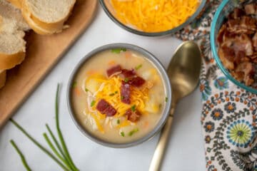 Bowl of potato soup topped with bacon, cheese, and chives.
