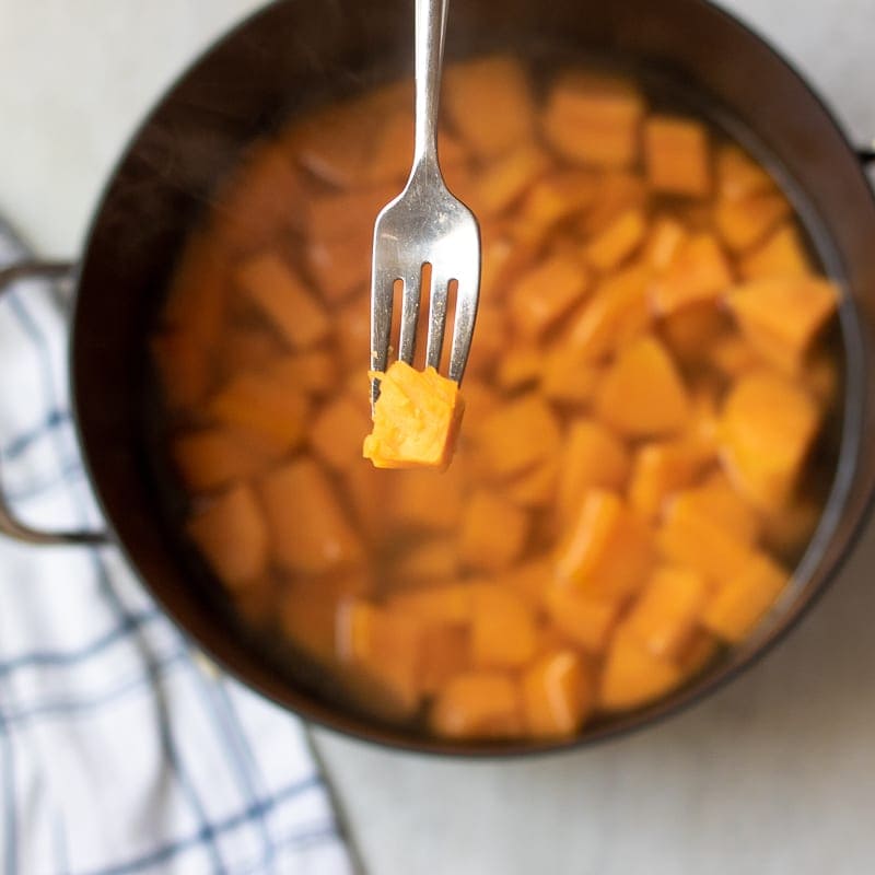 Sweet Potatoes chunk on fork over pot of cubed sweet potatoes. 