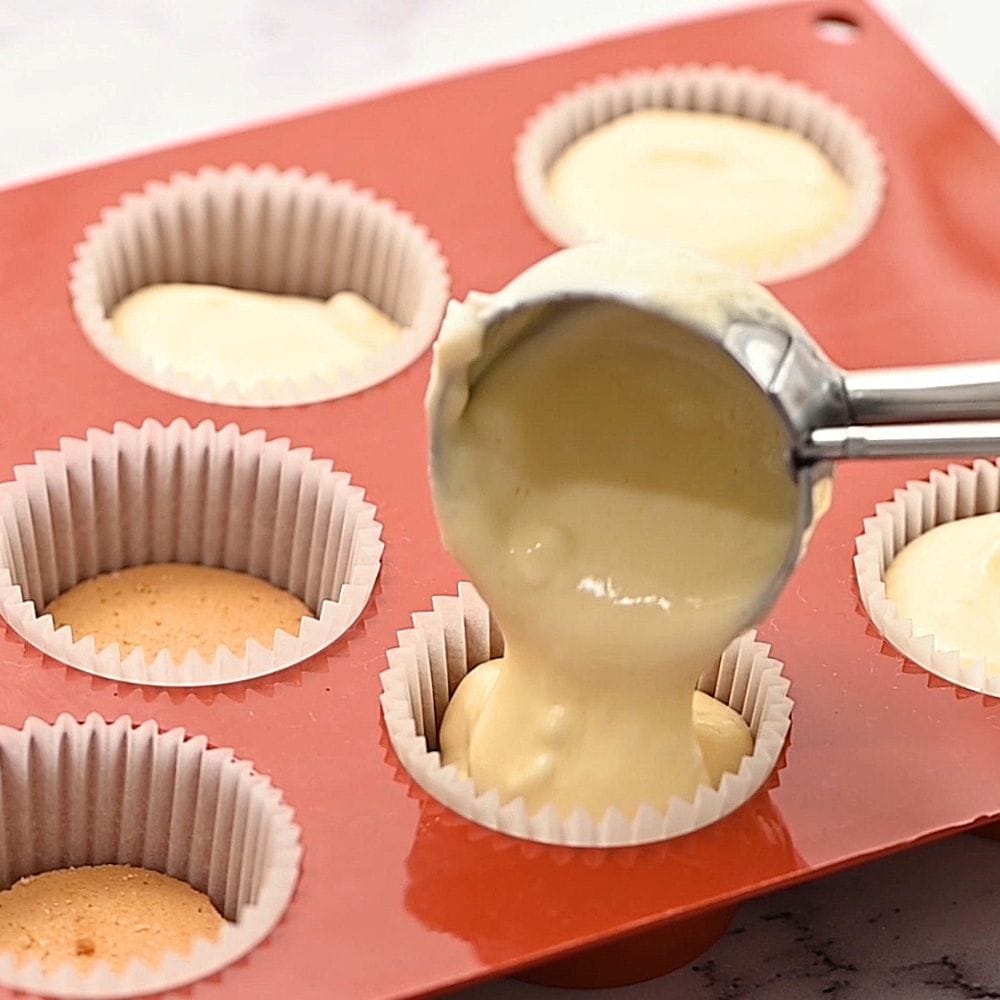 Mini cookie scoop scooping cheesecake batter into pan