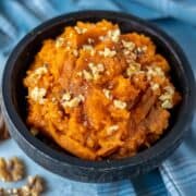 Bowl of Mashed Sweet Potatoes topped with walnuts, maple syrup and cinnamon