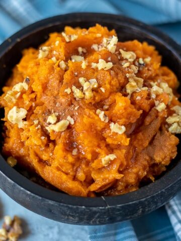 Bowl of Mashed Sweet Potatoes topped with walnuts, maple syrup and cinnamon
