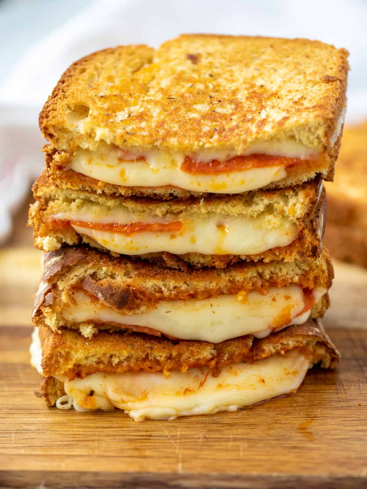 Stack of Pizza Grilled Cheese cut in half showing cheese oozing out on cutting board. 