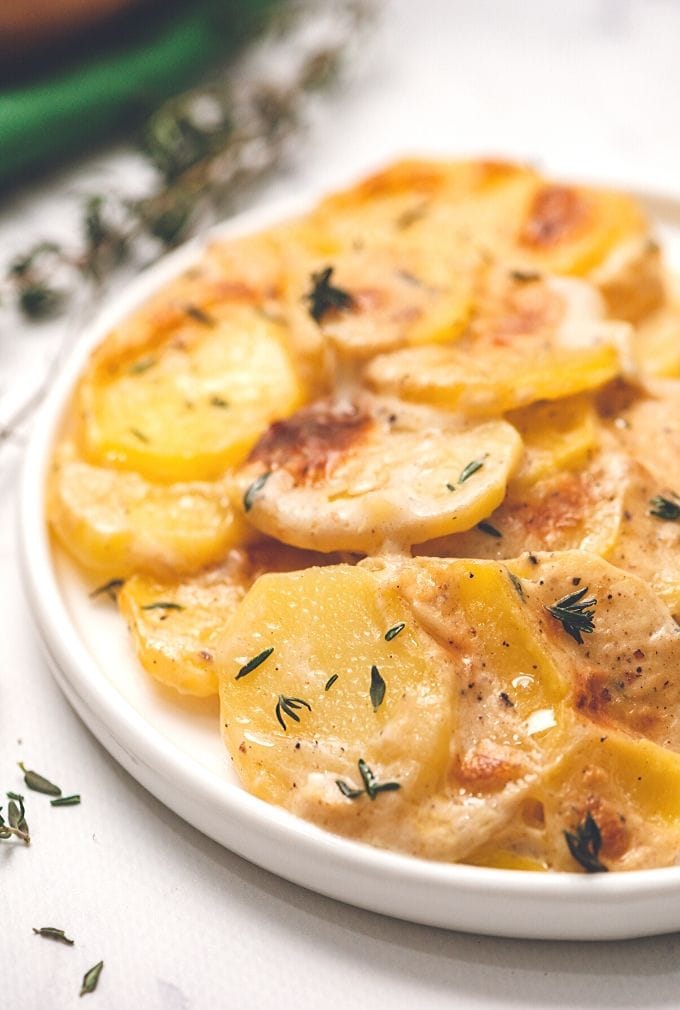 Plate with serving of Scalloped Potatoes next to fresh thyme.