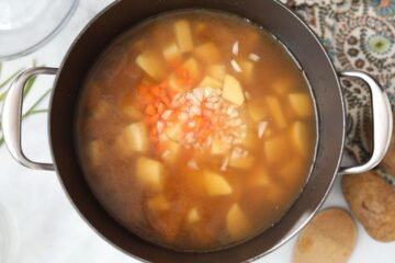 Potato, carrot, and onions in stockpan.