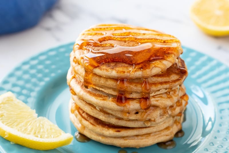 Pancakes stacked on blue plate topped with maple syrup.
