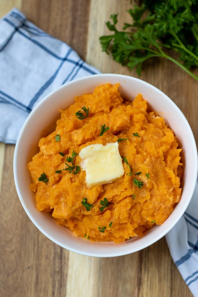 Bowl of Mashed Sweet Potatoes topped with butter and parsley.