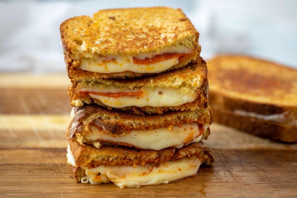 Sliced pizza grilled cheese sandwiches on cutting board. 