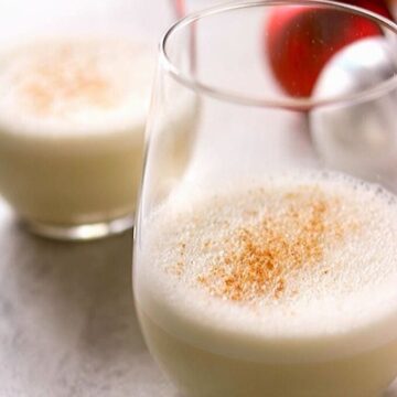 two glasses of coconut milk eggnog next to Christmas Ornaments