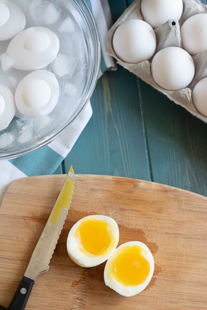 Sliced soft boiled egg on cutting board next to water bath.