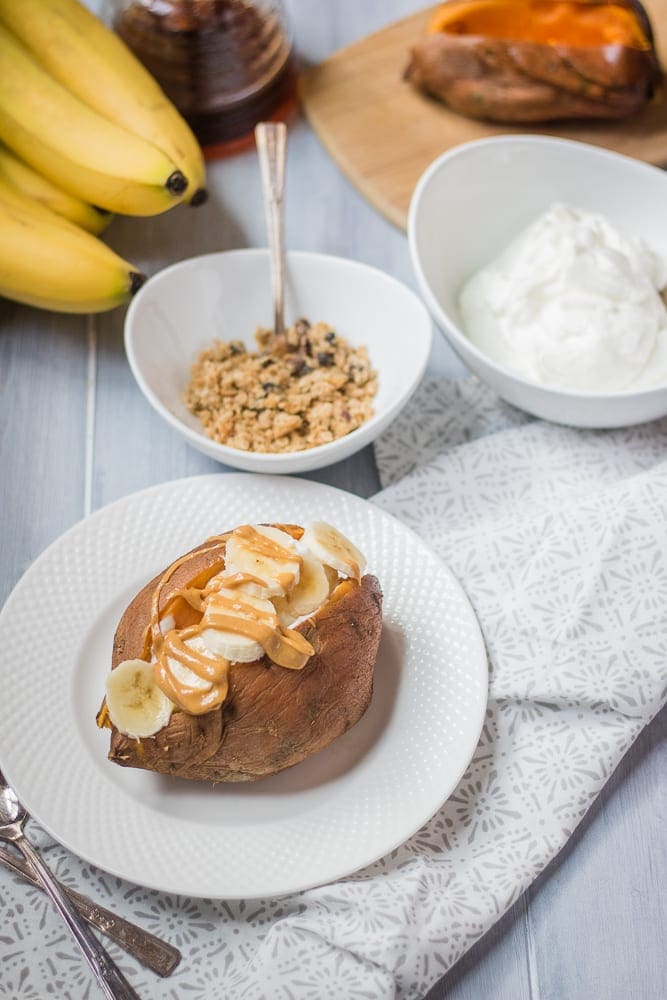 Baked Sweet Potato Topped with yogurt, banana, peanut butter with granola sitting to the side.