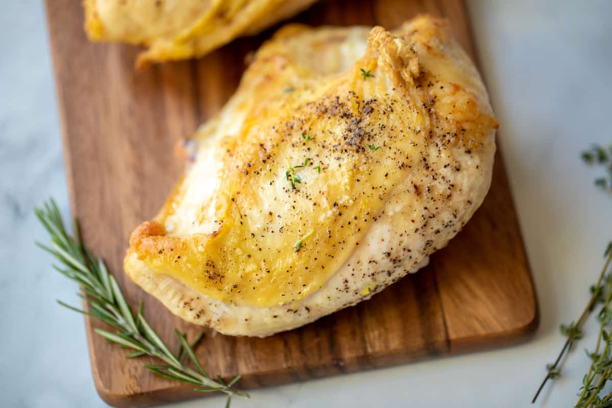 Baked Split Chicken Breast on cutting board next to rosemary.