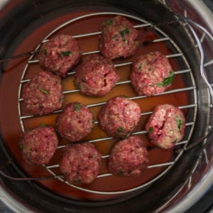 Uncooked meatballs in pressure cooker on trivet.