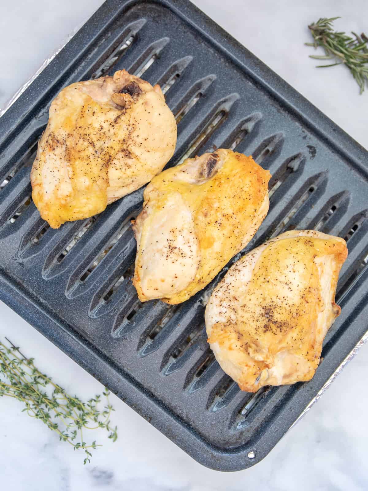 Roasted Split Chicken Breast on broiler pan next to fresh thyme.