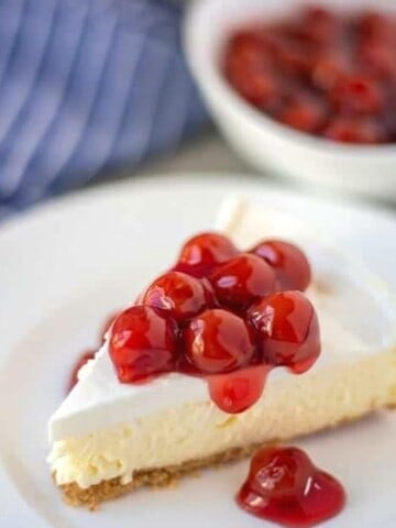 Slice of cheesecake with sour cream topping and cherries on white plate.